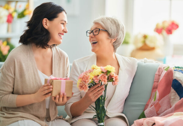 Happy mother's day! Child daughter is congratulating mom and granny giving them flowers and gift. Grandma, mum and girl smiling and hugging. Family holiday and togetherness.
