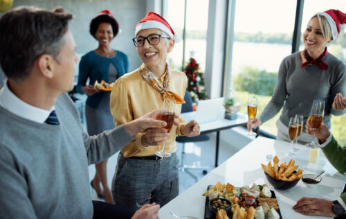 Happy mature businesswoman having glass of Champagne while celebrating with colleagues on Christmas party in the office.