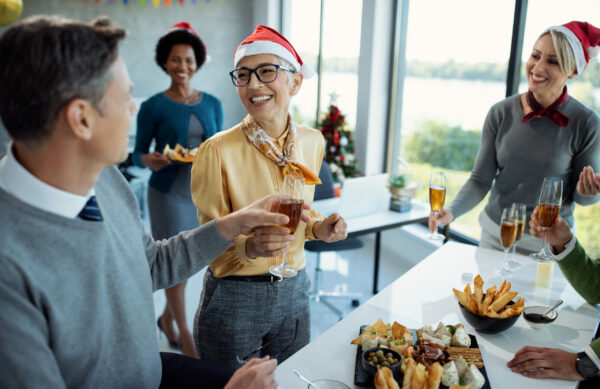 Happy mature businesswoman having glass of Champagne while celebrating with colleagues on Christmas party in the office.