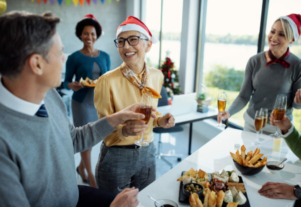 Happy mature businesswoman having glass of Champagne while celebrating with colleagues on Christmas party in the office.